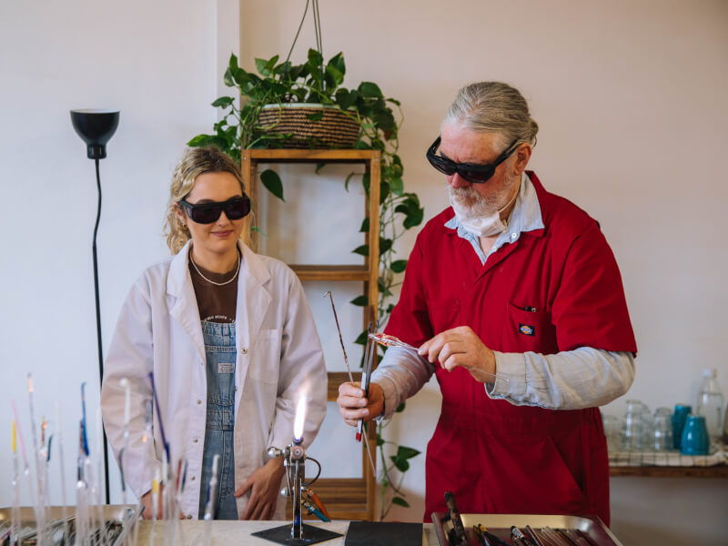 A man showing a woman how to silversmith at a craft class.